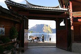 Mosuo man and horse with Gemu Goddess Mountain and Lugu Lake through ornate gate, Luoshui village